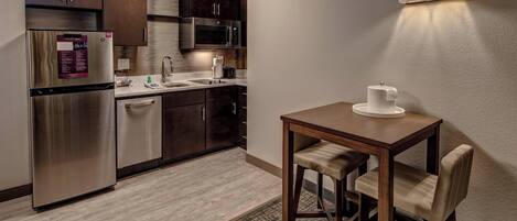 Cocina compacta con armarios de madera oscura, electrodomésticos de acero inoxidable y una pequeña mesa de comedor con dos sillas.