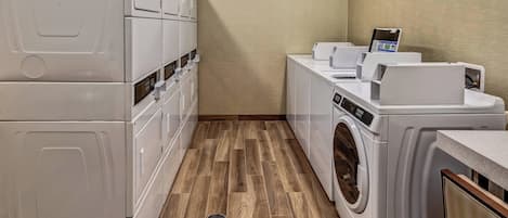 A laundry room with stacked washer-dryer units, a clock on the wall, and a small table with a device on it.