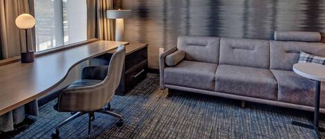 A hotel room with a desk, office chair, sofa, and a small table.