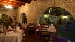 Un restaurant aux murs de pierre, avec des tables et des chaises en bois. On y trouve des plantes et un extincteur accroché au mur.