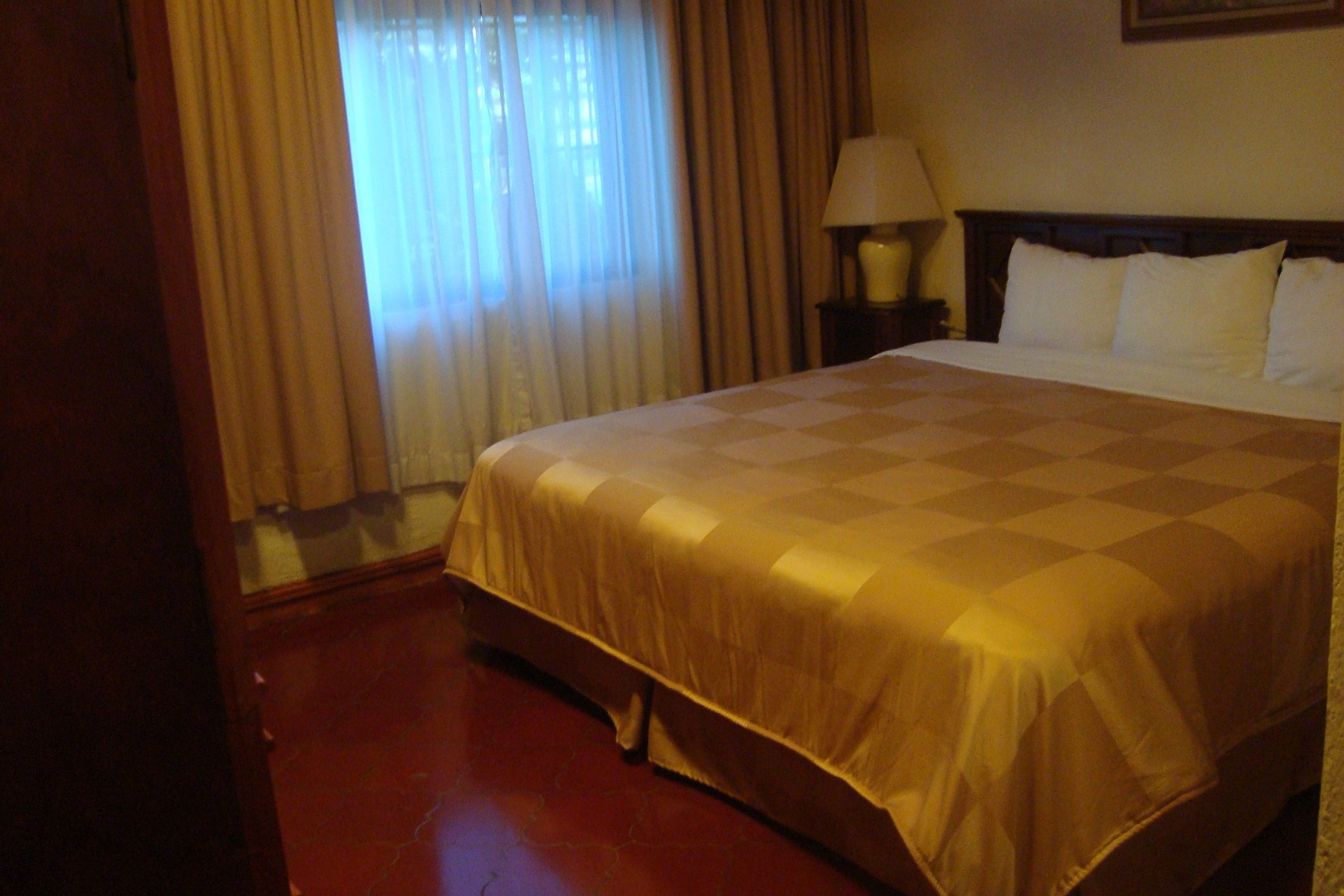 Una camera d'albergo con un letto grande, un comodino con una lampada e una finestra con tende.