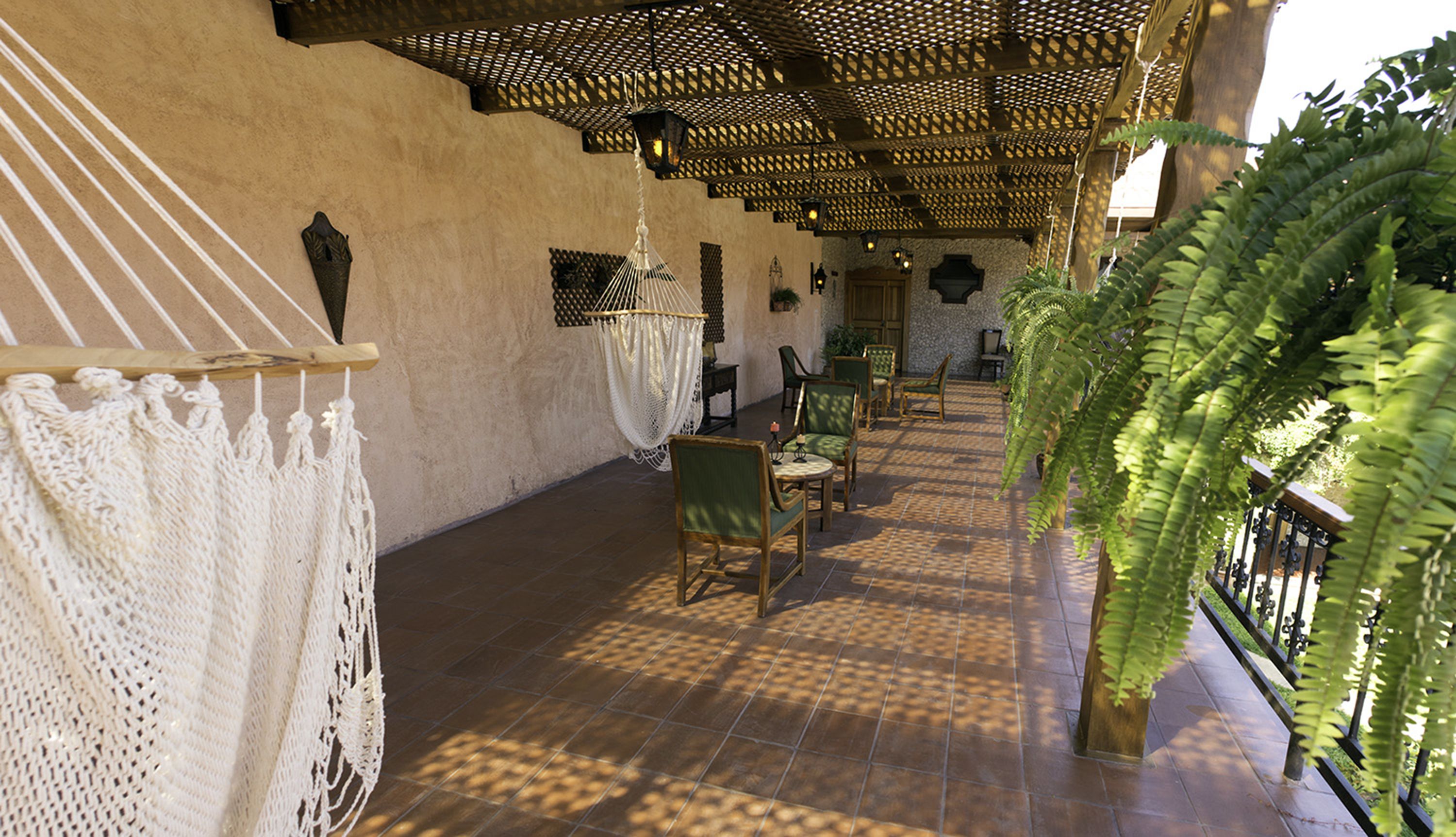 A covered patio area with a tiled floor, wicker furniture, and a large fern plant.