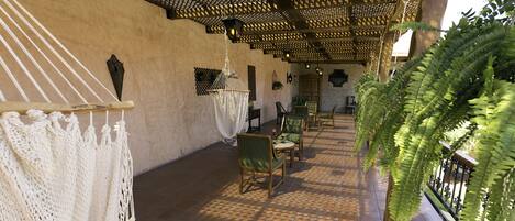 A covered patio area with a tiled floor, wicker furniture, and a large fern plant.