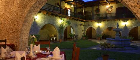 An outdoor dining area with stone arches, a fountain, and potted plants.