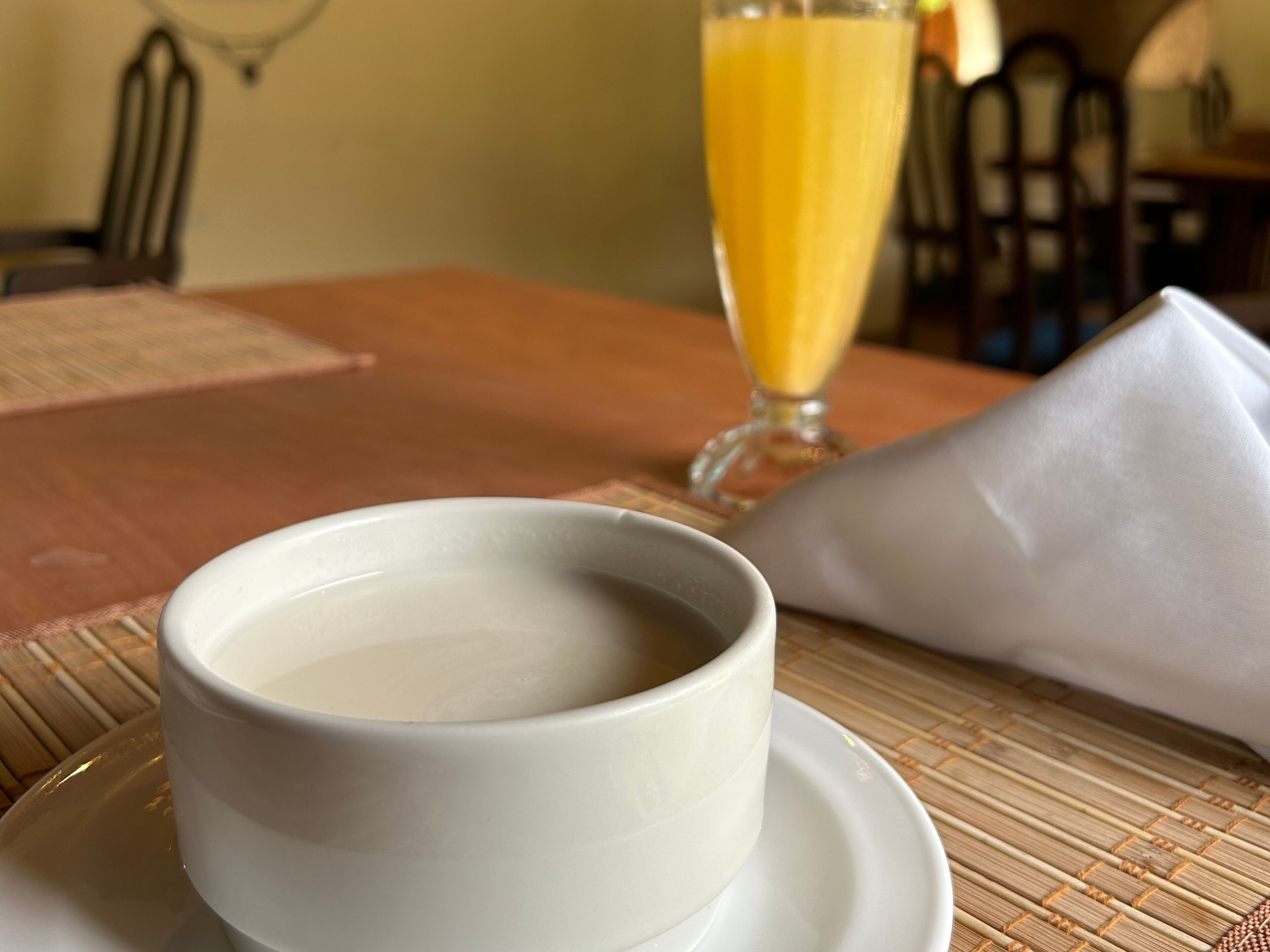 Una taza blanca sobre un plato, un vaso de jugo de naranja y una servilleta doblada en una mesa.