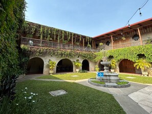 A courtyard with a fountain, arched doorways, and a balcony with plants. - Hotel Del Patio (Flores)