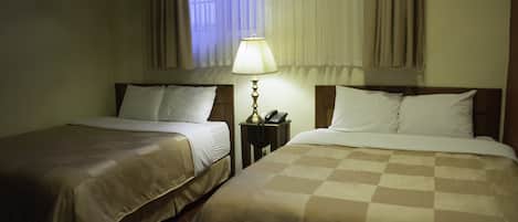 Een hotelkamer met twee bedden, een nachtkastje met lamp en een raam met gordijnen.