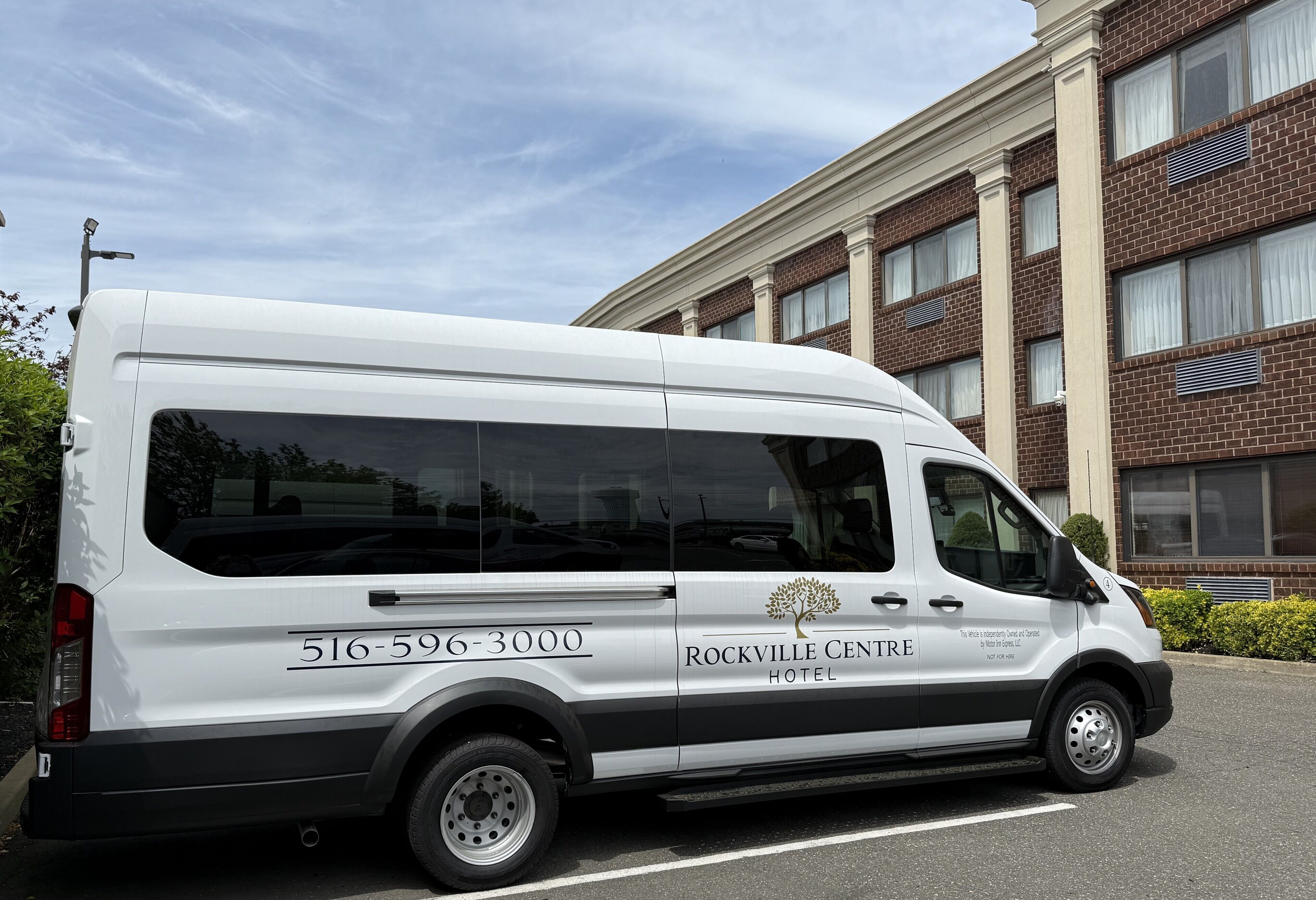 Una camioneta blanca estacionada frente a un edificio con la inscripción 'Rockville Center Hotel' y el número de teléfono '516-596-3000'.