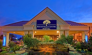 El exterior del Hotel Rockville Centre, con un cartel llamativo, fachada de piedra y una entrada ajardinada.