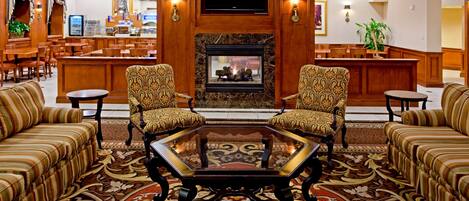 A lobby with a fireplace, two armchairs, a coffee table, and a bar area with seating.