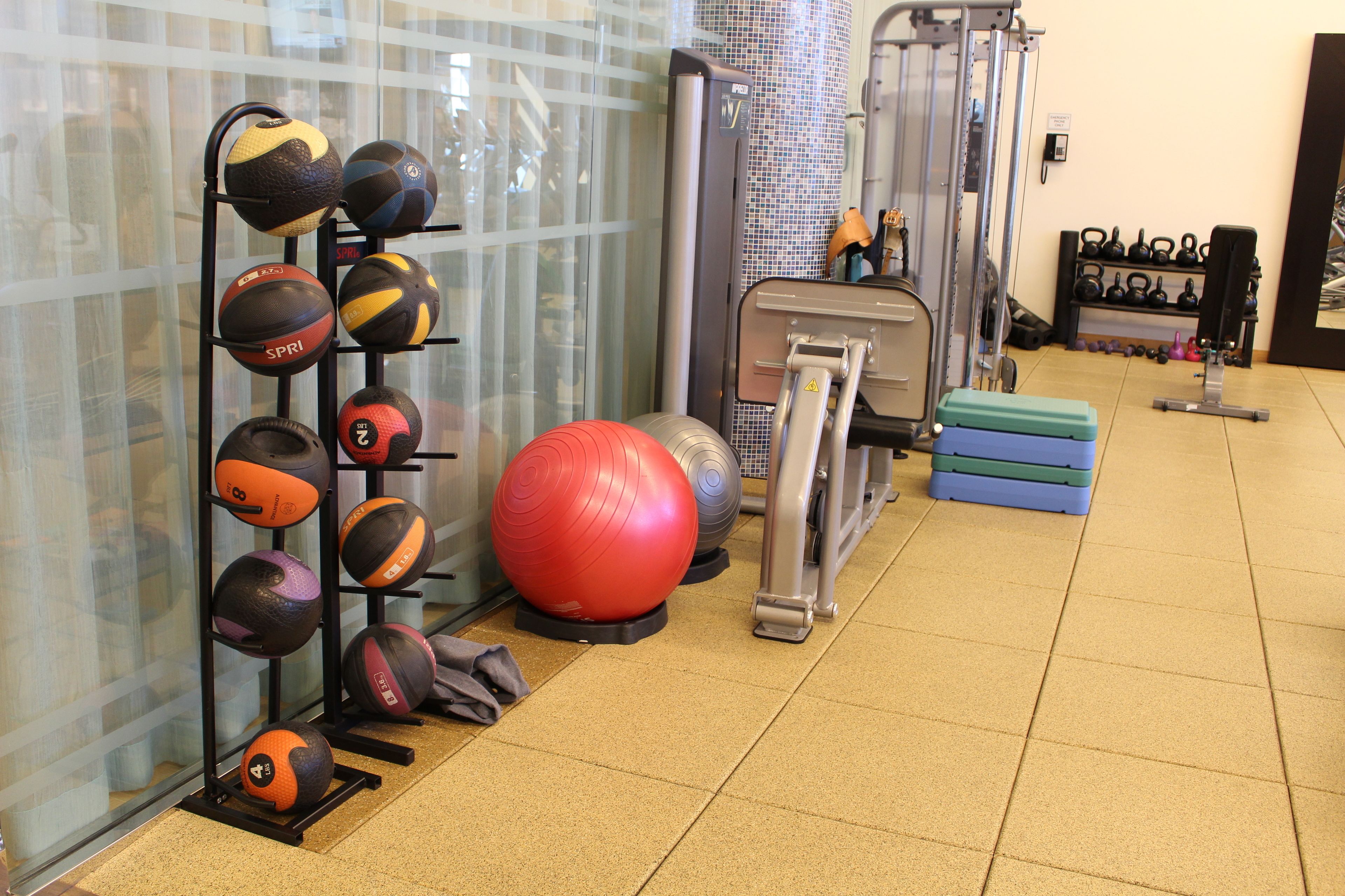Un gimnasio con equipo de ejercicio, un estante de balones deportivos y un set de kettlebells.