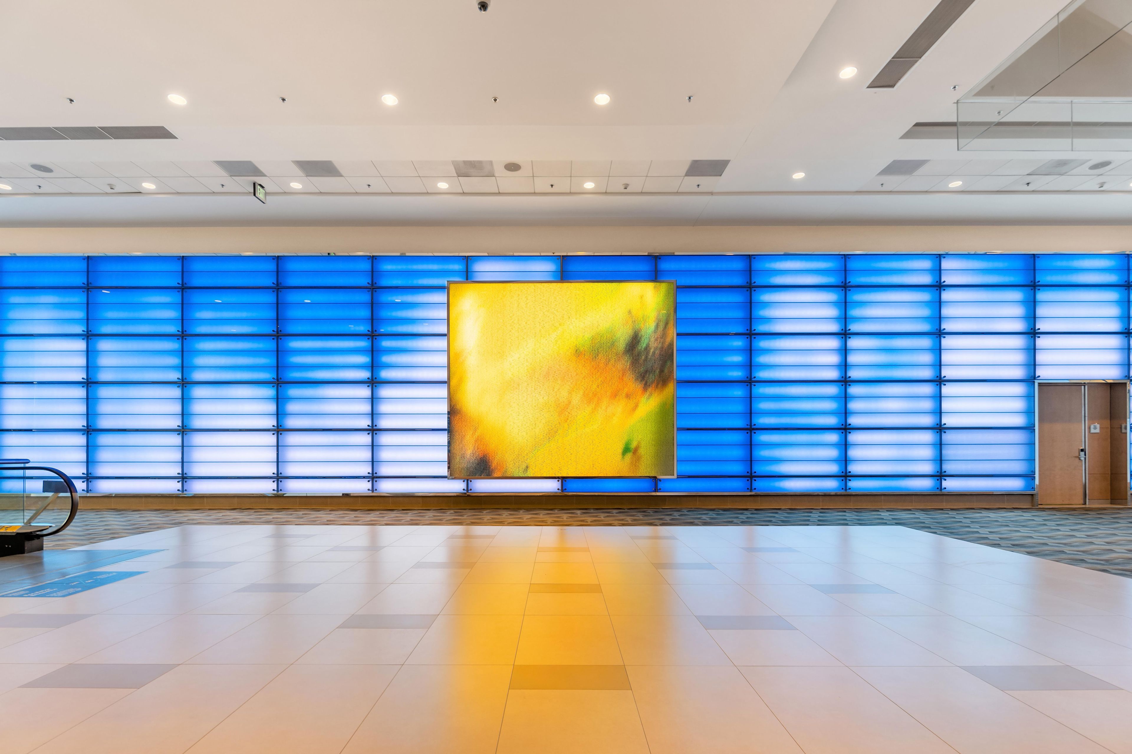 Un vestíbulo amplio con una gran instalación de arte abstracto, una pared con diseño azulado y suelo de baldosas.