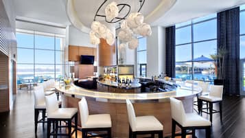 A modern bar area with a curved counter, bar stools, and a large window offering a view of the cityscape.