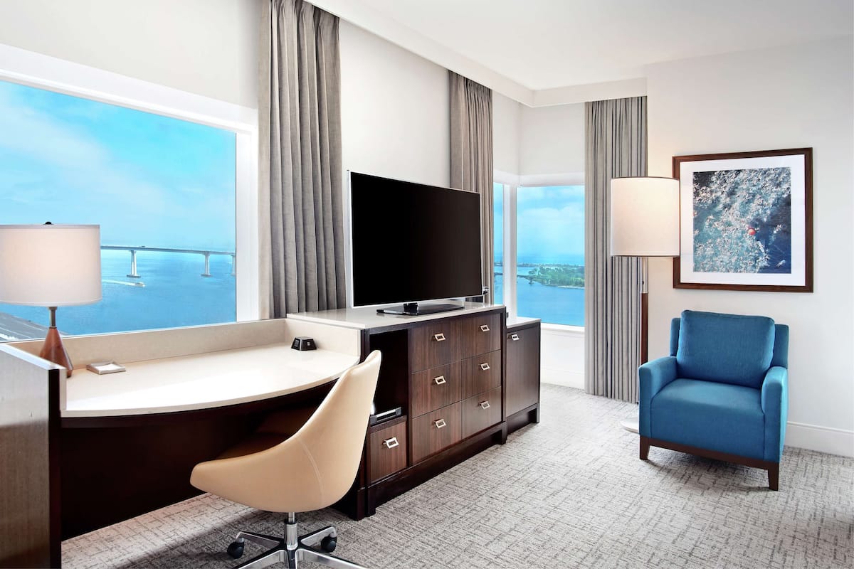 A hotel room with a desk, chair, television, and a view of a bridge.