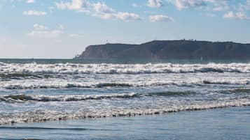 Paisaje costero con olas, cielo despejado y una colina distante con construcciones.
