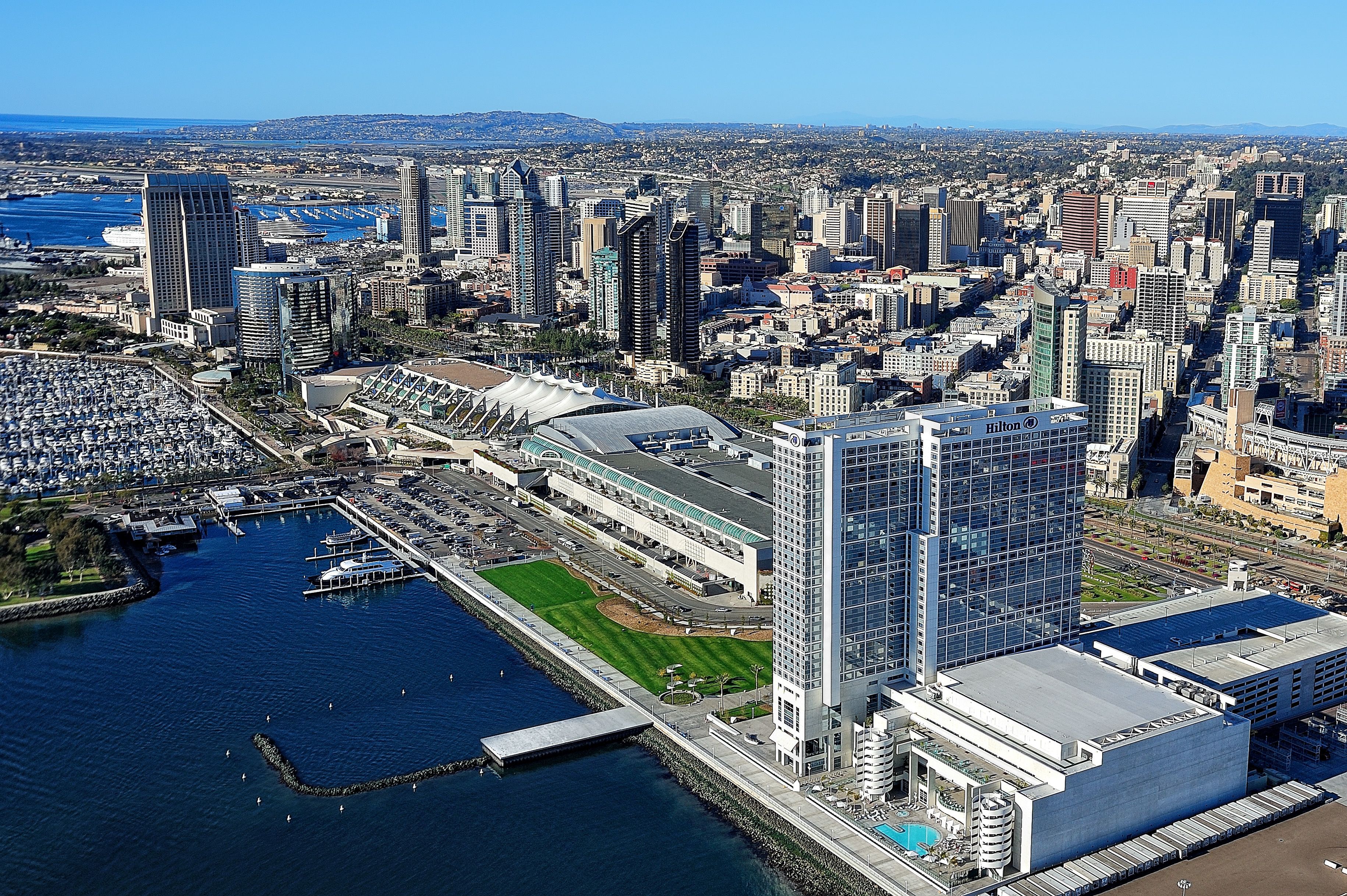 Un hotel moderno de gran altura con fachada de vidrio, cerca de un puerto deportivo con barcos amarrados.