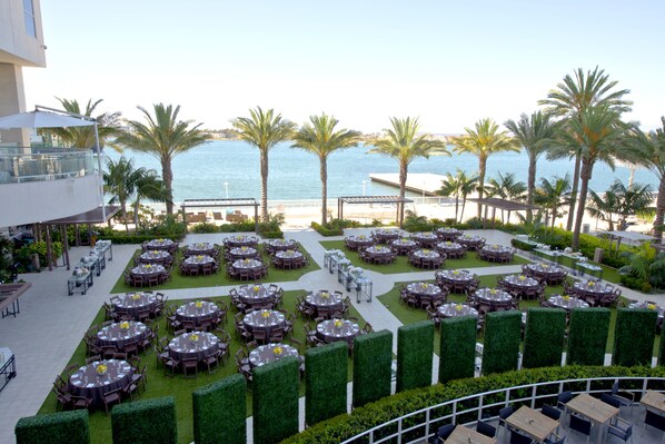A rooftop dining area with multiple round tables, palm trees, and a view of the sea. - Hilton San Diego Bayfront (San Diego)