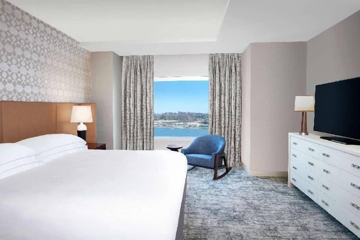 A hotel room with a bed, a chair, a TV, a dresser, and a view of the ocean.