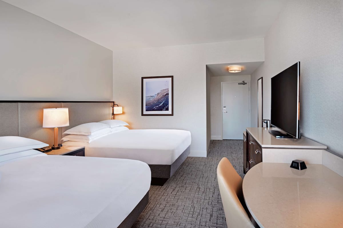A hotel room with two beds, a desk, a television, and a framed picture on the wall.