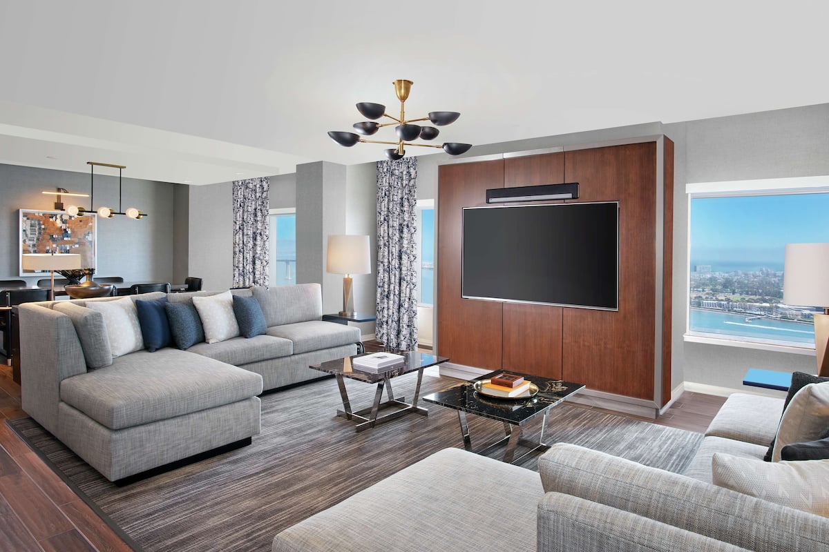 A modern living room with a grey sectional sofa, a coffee table, and a flat-screen TV mounted on a wooden wall.