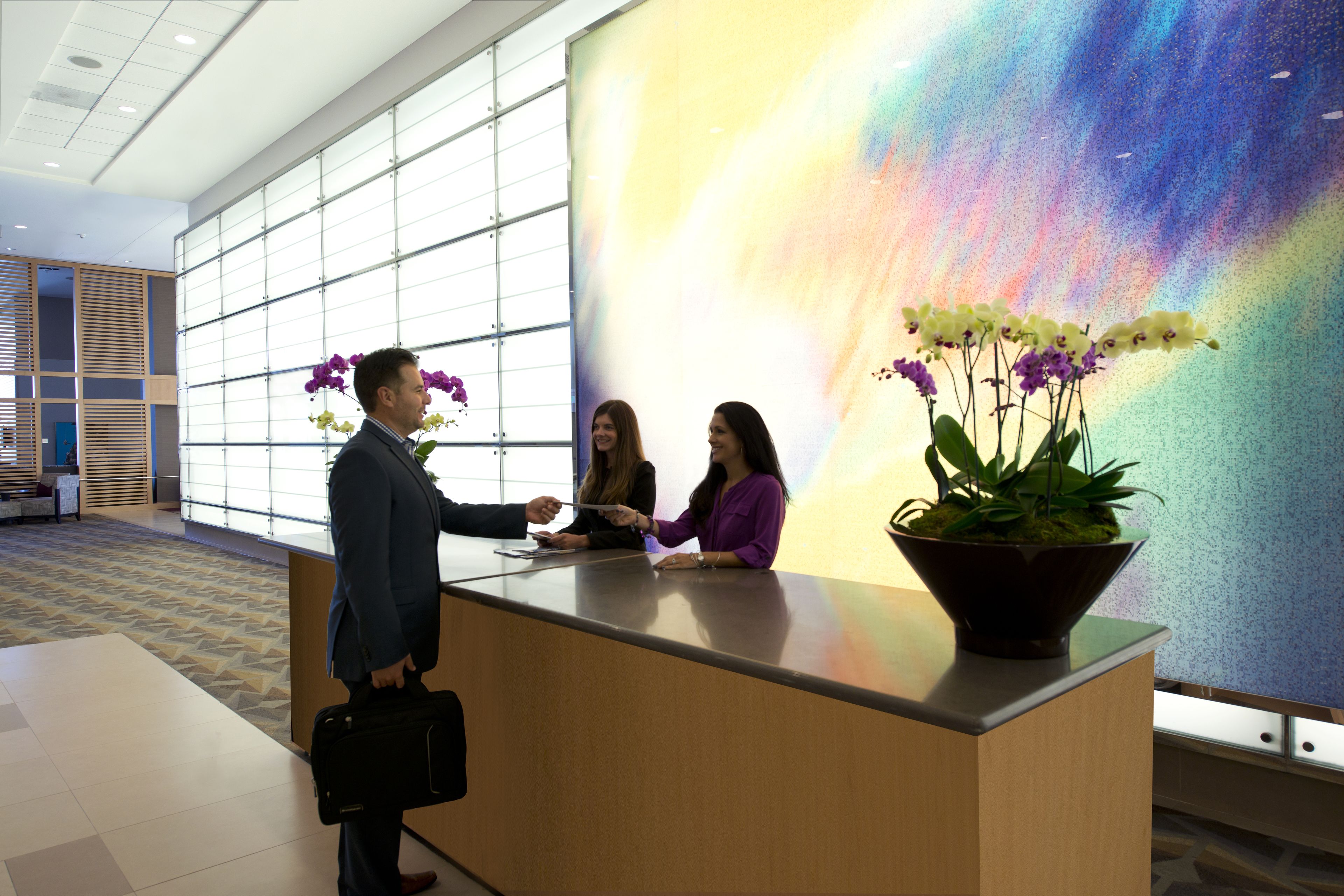 A reception desk with a large window, a potted plant with orchids, and a colorful abstract mural in the background.