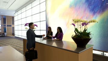 A reception desk with a large window, a potted plant with orchids, and a colorful abstract mural in the background.