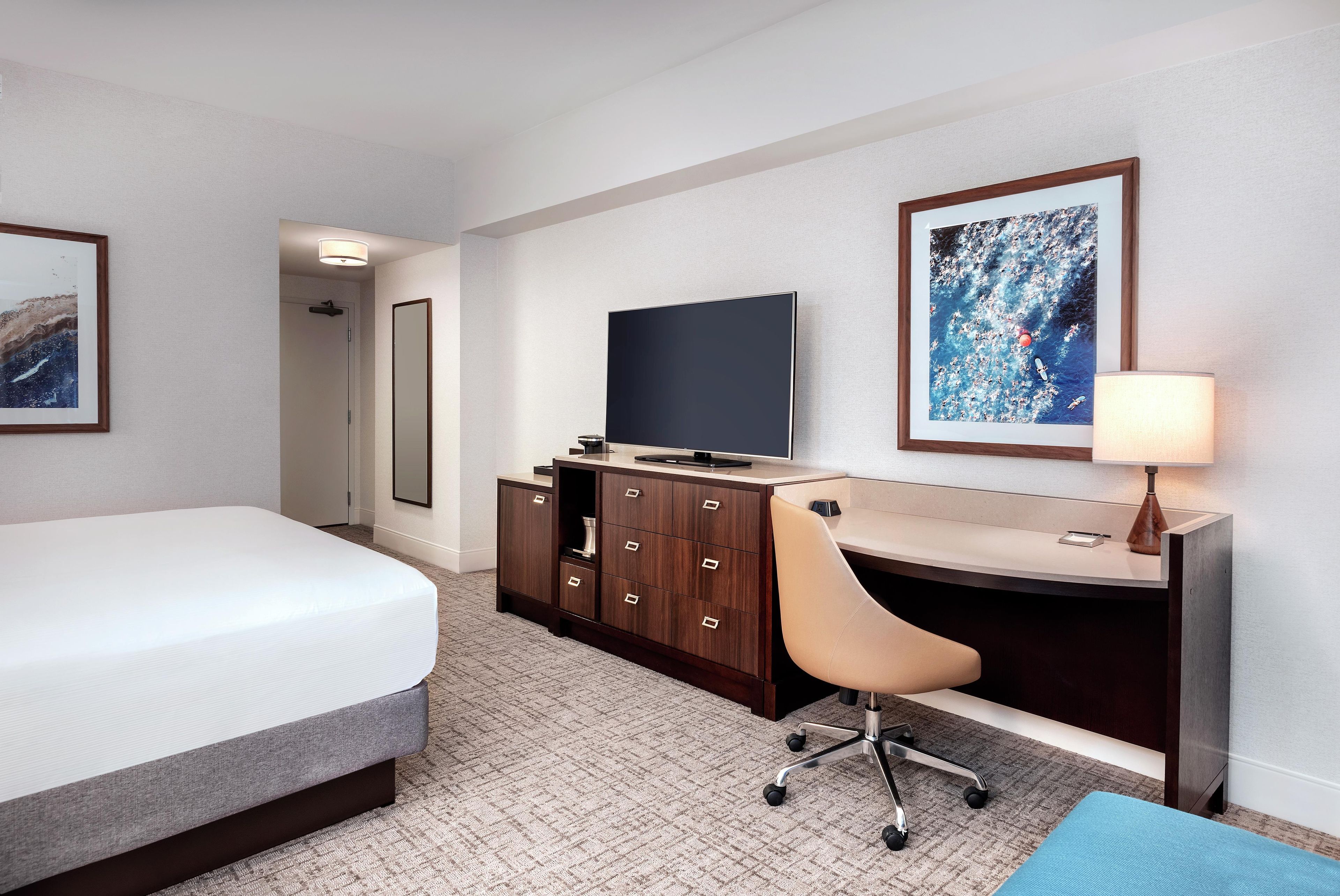 A hotel room with a bed, a desk, a chair, a television, and artwork on the walls.