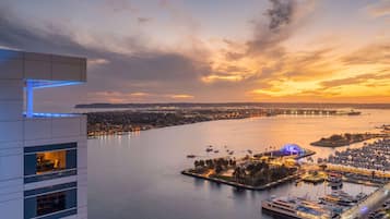 Vista para a frente marítima com um porto de iates, um edifício grande com varandas e um pôr do sol sobre a água.