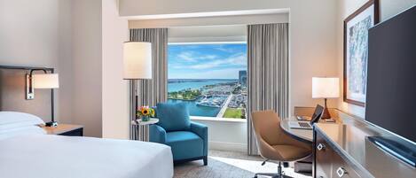 Habitación de hotel con cama, escritorio, silla, televisión y vistas a la ciudad y al agua.