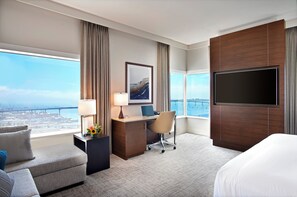 Une chambre d’hôtel avec un grand lit, un bureau avec un ordinateur portable, une chaise, une télévision et une vue sur un pont et sur l’eau.