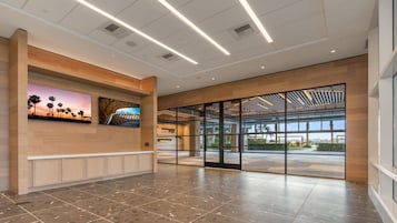 Eine großzügige Lobby mit einer Rezeption, einem an der Wand befestigten Fernseher und einer großen Glasdoor, die nach draußen führt.