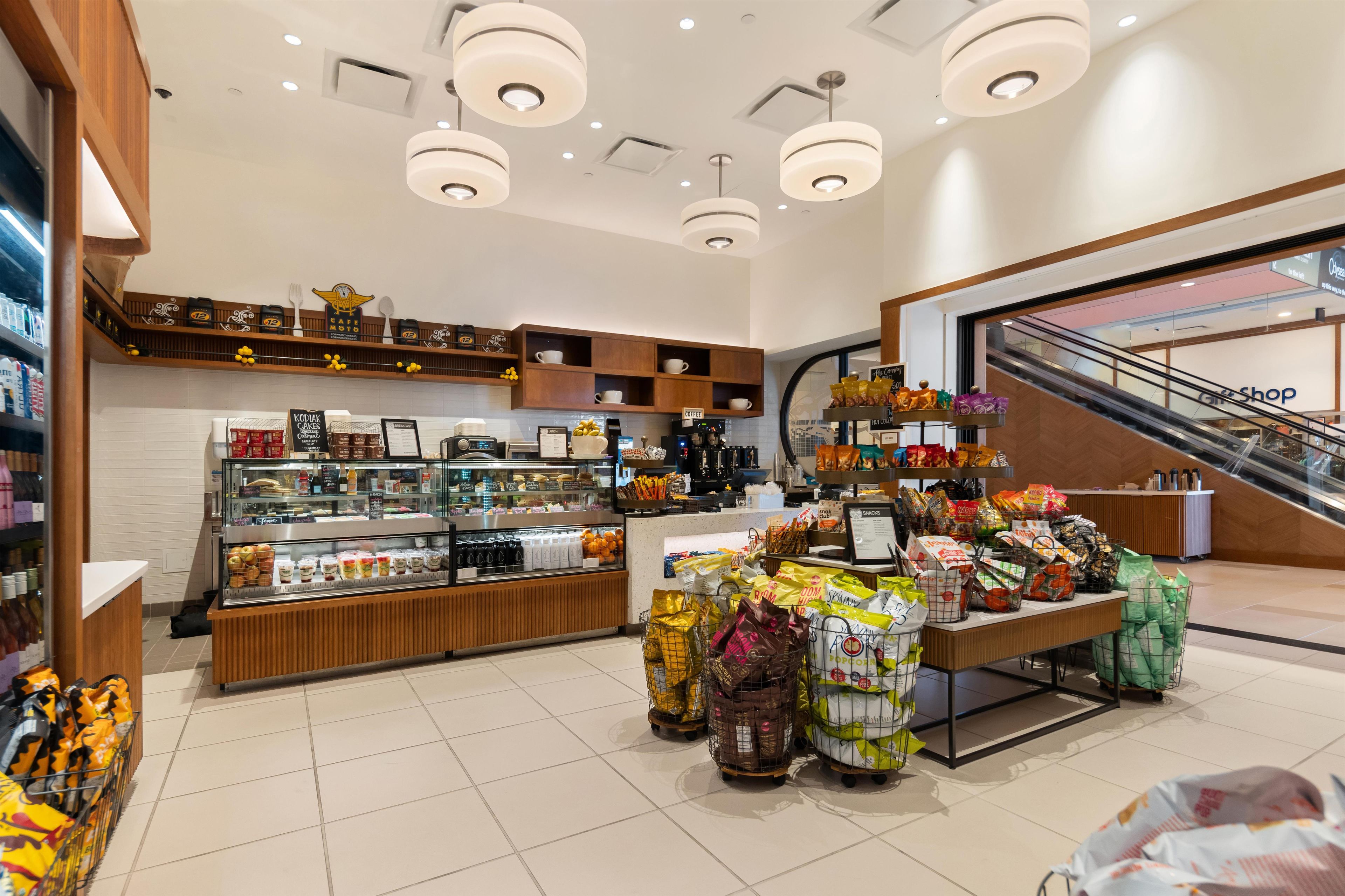 A modern cafe with a variety of food and drink options, including a bakery display and a coffee station.