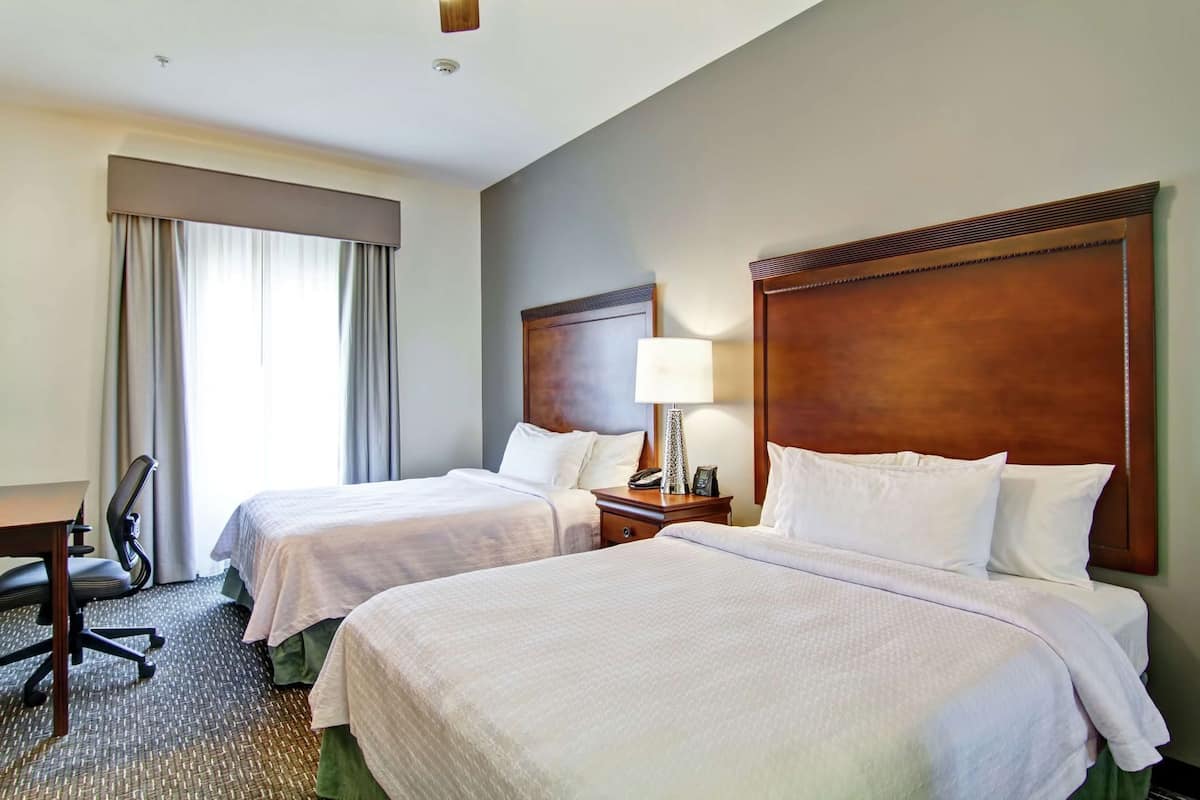 A hotel room with two beds, a desk, a chair, a lamp, and a phone on the nightstand.