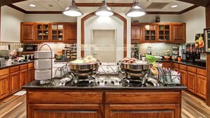 A kitchen with wooden cabinets, a central island with buffet bowls, and pendant lighting.