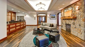 A spacious lobby with a stone fireplace, a reception desk, and a comfortable seating area with a coffee table and ottomans.