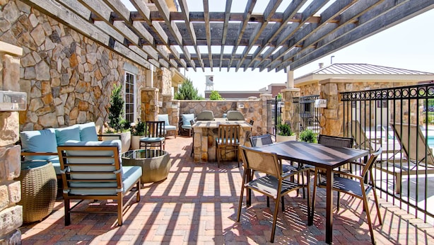 A covered patio area with stone walls, a stone fireplace, outdoor furniture, and a pool in the background.