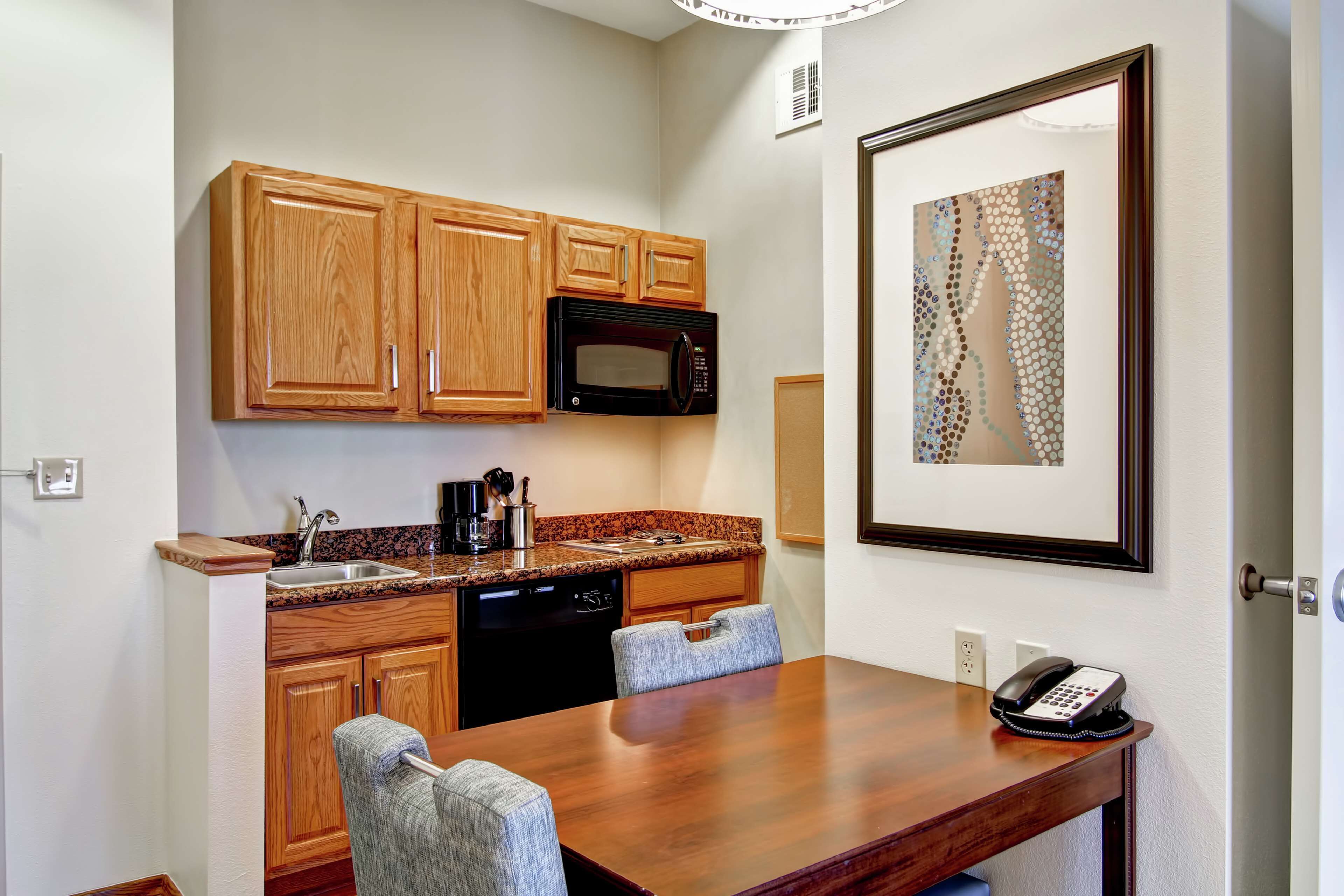 A compact kitchen with wooden cabinets, a microwave, a sink, and a dining table with chairs.