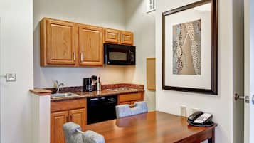 A compact kitchen with wooden cabinets, a microwave, a sink, and a dining table with chairs.