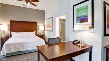 A hotel room with a bed, a desk, a chair, a phone, and a ceiling fan.