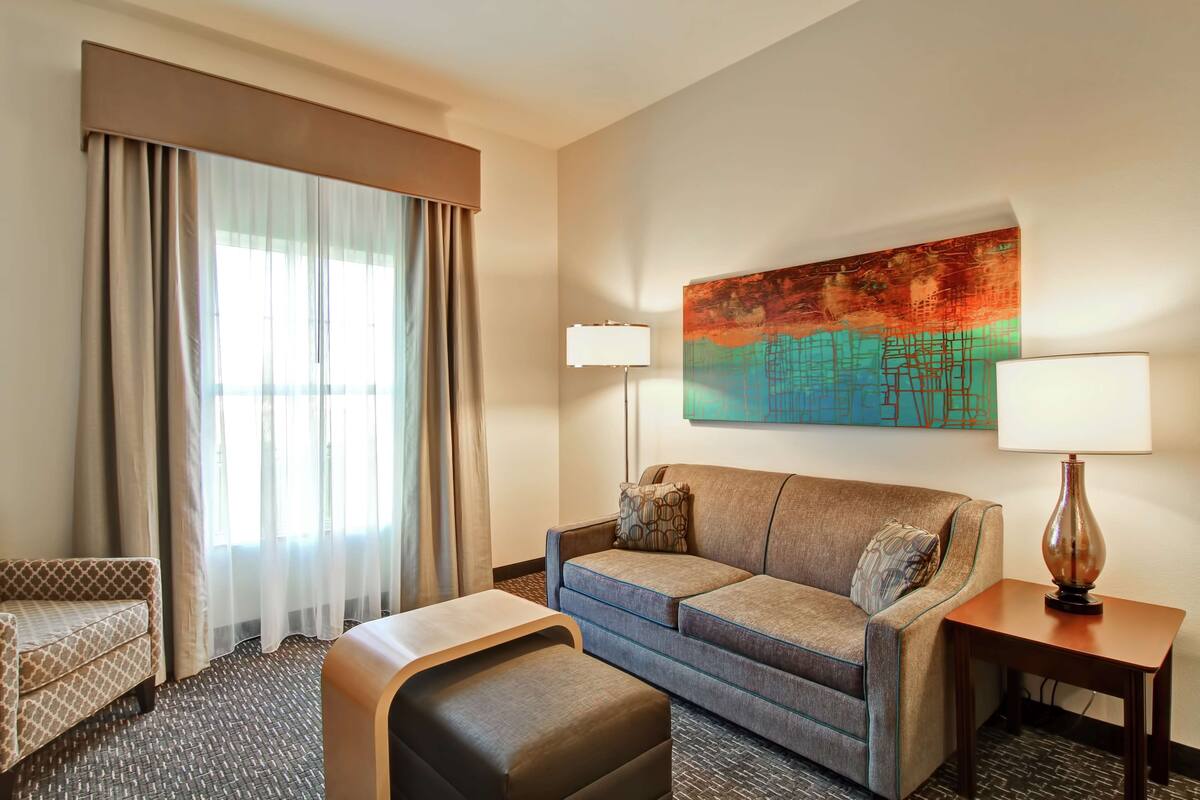 A hotel room with a sofa, a small table, a lamp, and a painting on the wall.