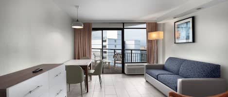 A modern hotel room with a dining area, a sofa, and a balcony with a view of buildings.