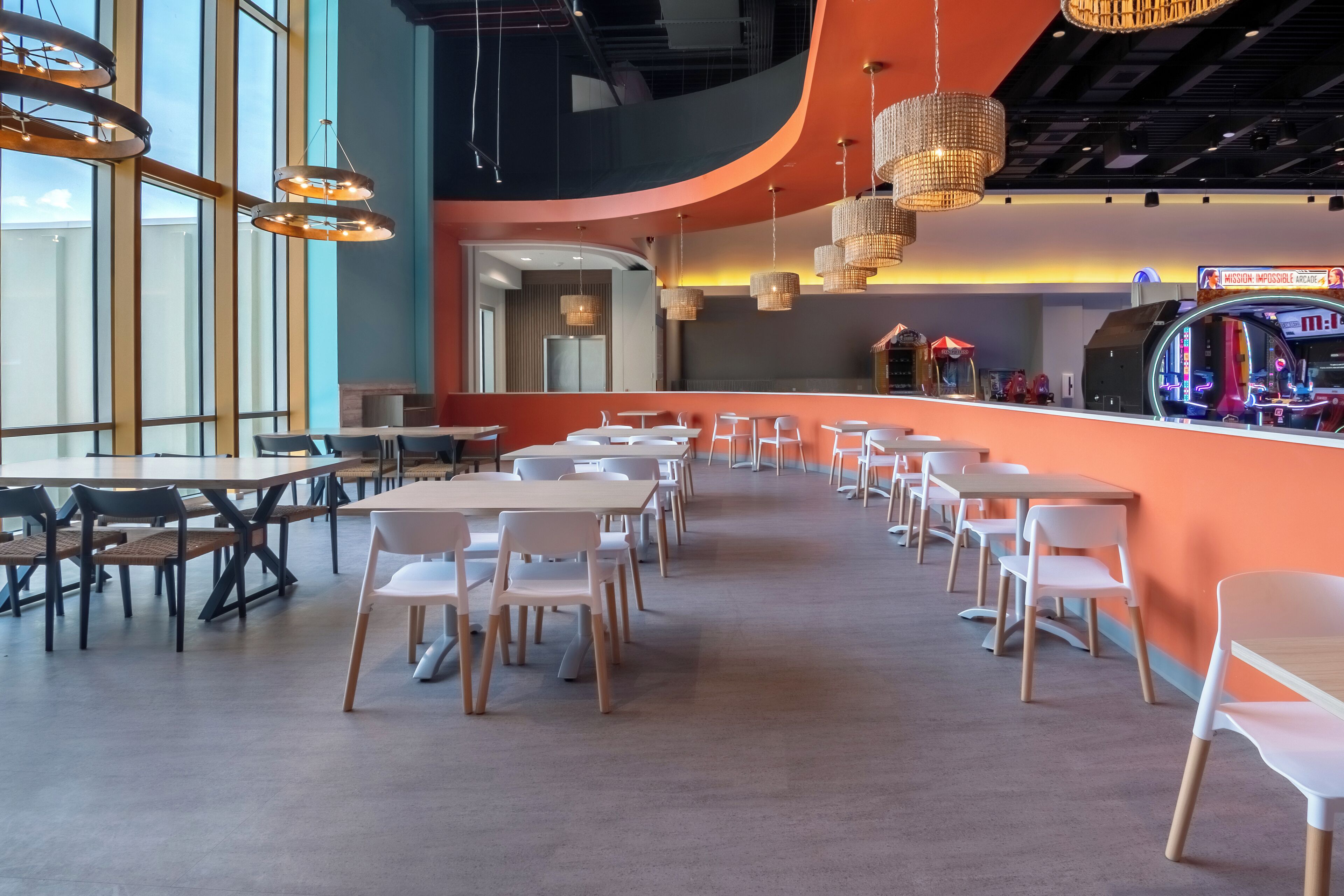 A modern dining area with tables and chairs, a counter with arcade machines, and pendant lighting.