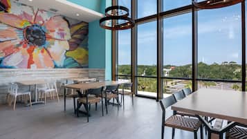 A modern dining area with large windows, a colorful mural, and contemporary furniture.