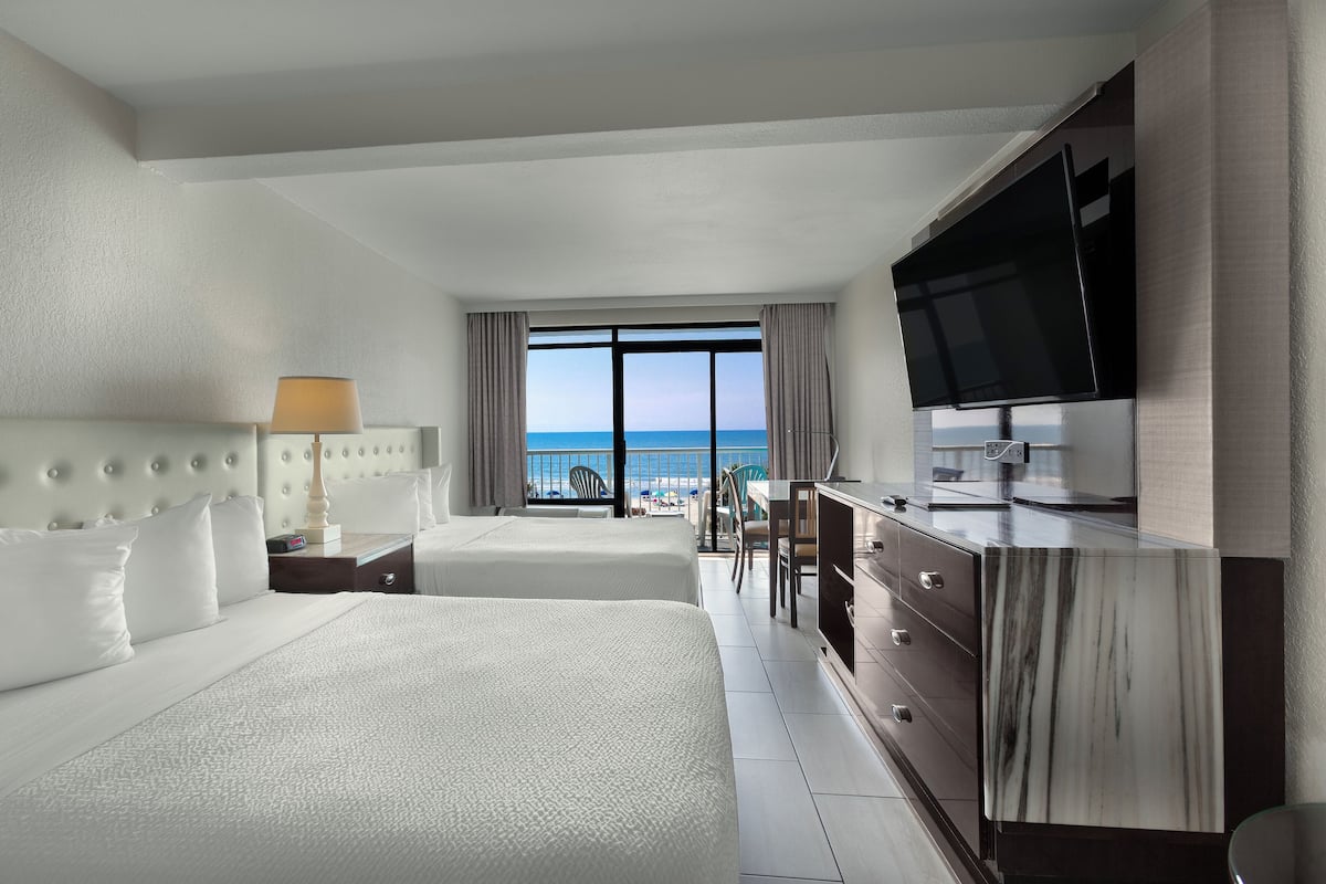 A hotel room with a large bed, a TV, a desk, and a view of the ocean.