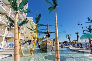 A pool area with a ship-shaped water feature, palm trees, and a building with balconies.