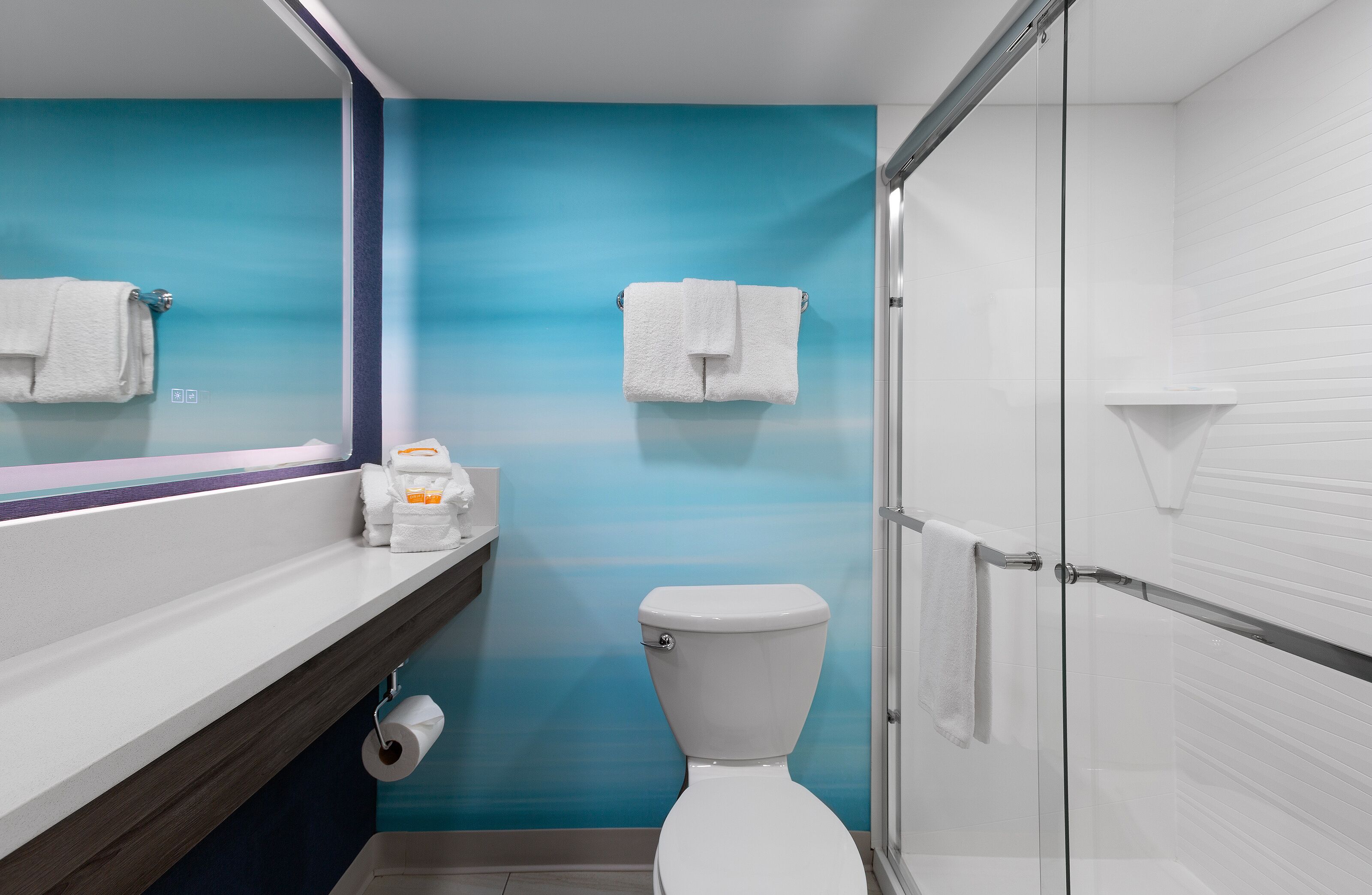 Un baño con pared de gradiente azul, un inodoro blanco, una cabina de ducha de vidrio y un espejo.