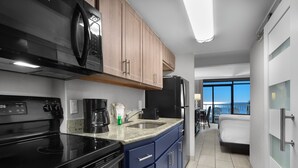 A modern kitchen with a black stove, a coffee maker, and a sink. There is a balcony with a view of the sky. - Captain's Quarters Resort (Myrtle Beach)