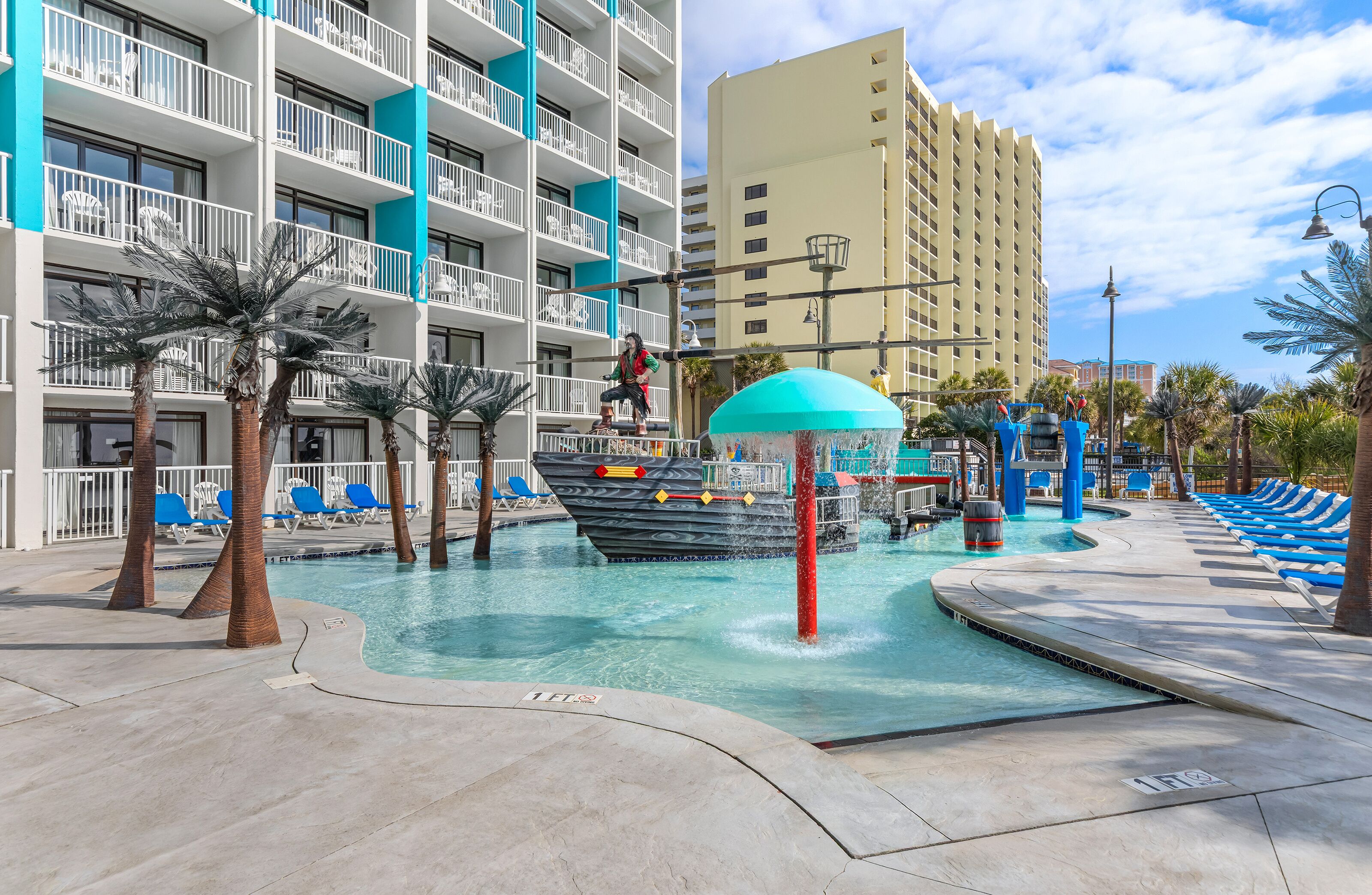 A hotel pool area with a water slide, lounge chairs, and a building with balconies.