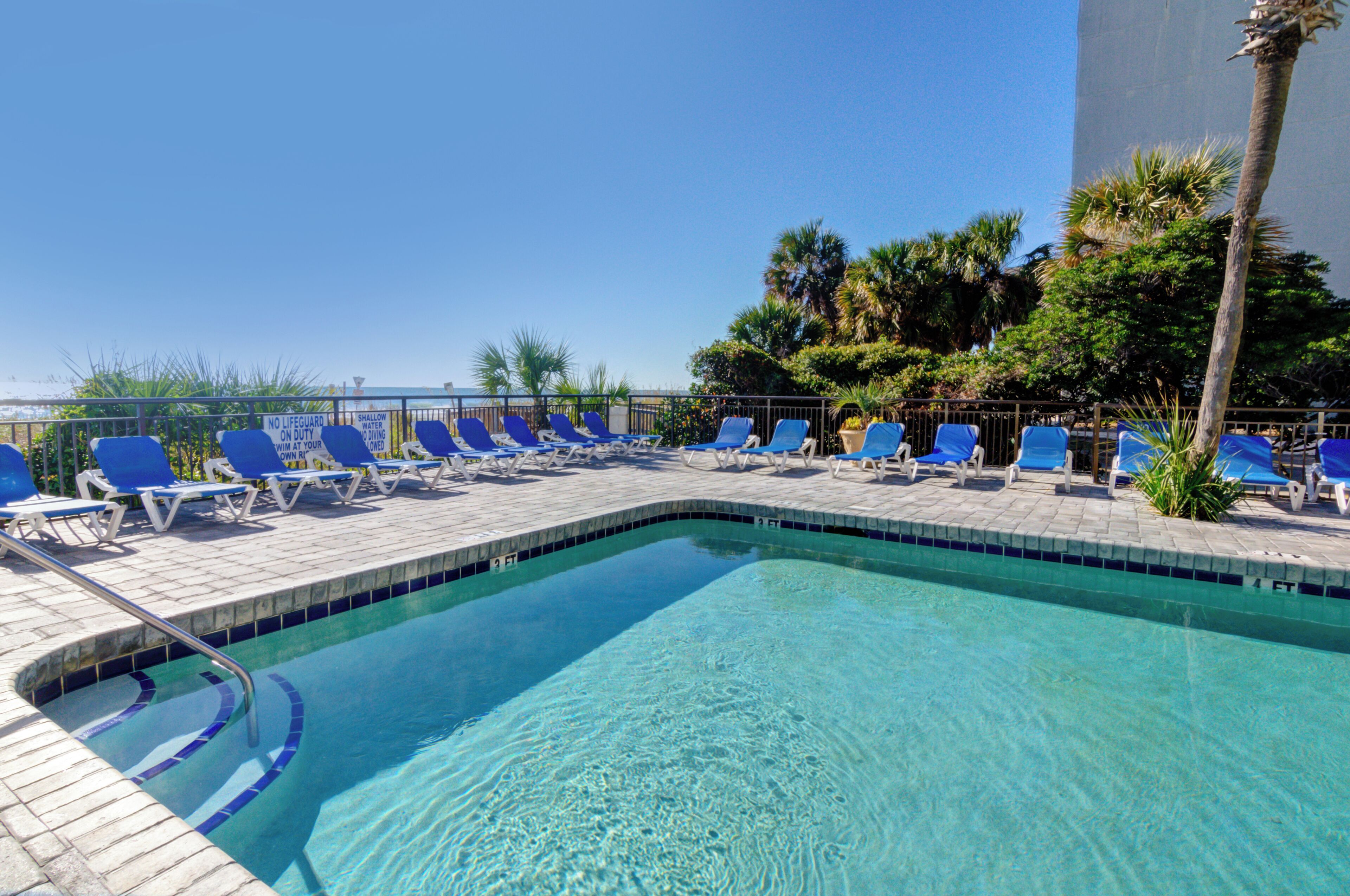 A pool area with blue lounge chairs and a clear blue pool.