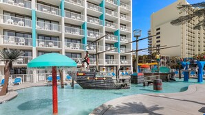 A pool area with a ship-shaped water feature, lounge chairs, and a multi-story building with balconies. - Captain's Quarters Resort (Myrtle Beach)